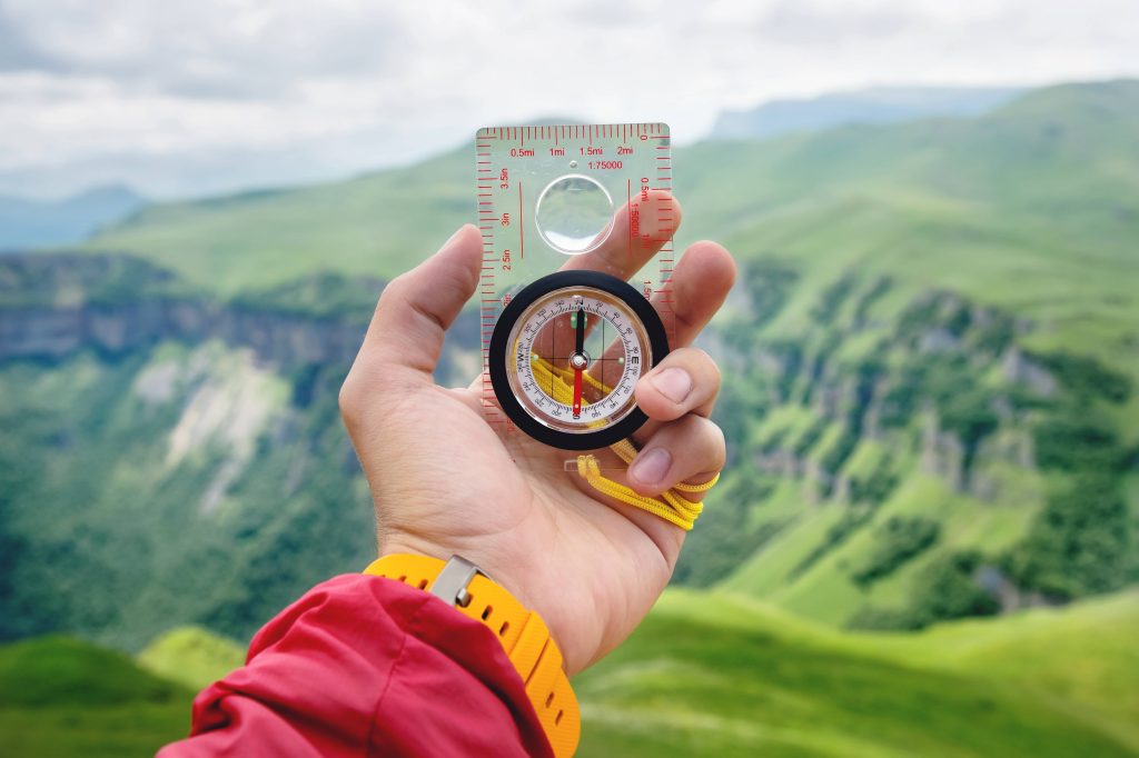 Male hand is holding a magnetic compass on the background of hills and the sky with clouds