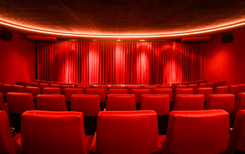 Ein leerer Kinosaal, rote Sitze, rote Wände, roter Vorhang vor der Leinwand