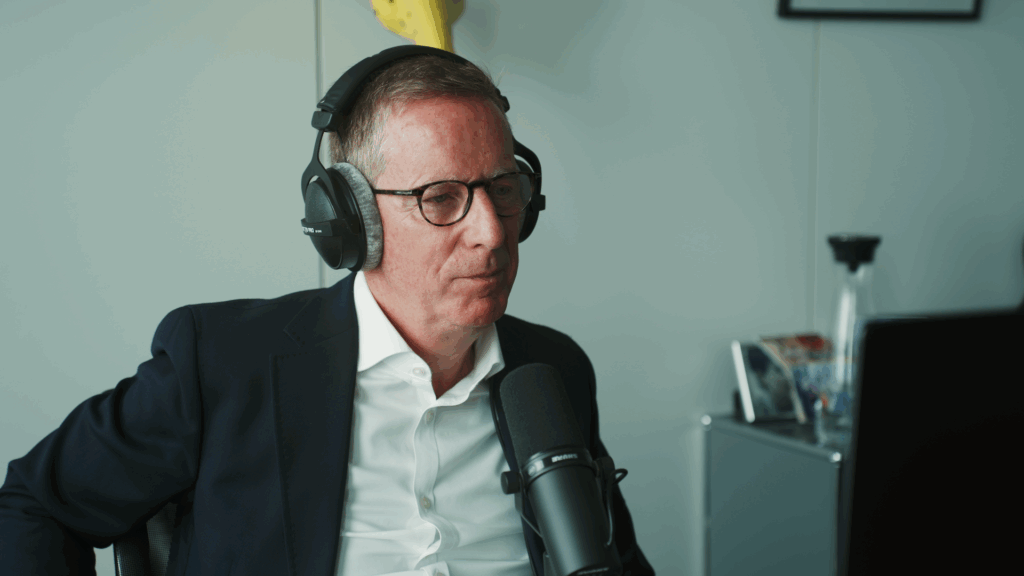 Eine Person mit Kopfhörern in Hemd und Blazer sitzt an einem Mikrofon und hört zu.