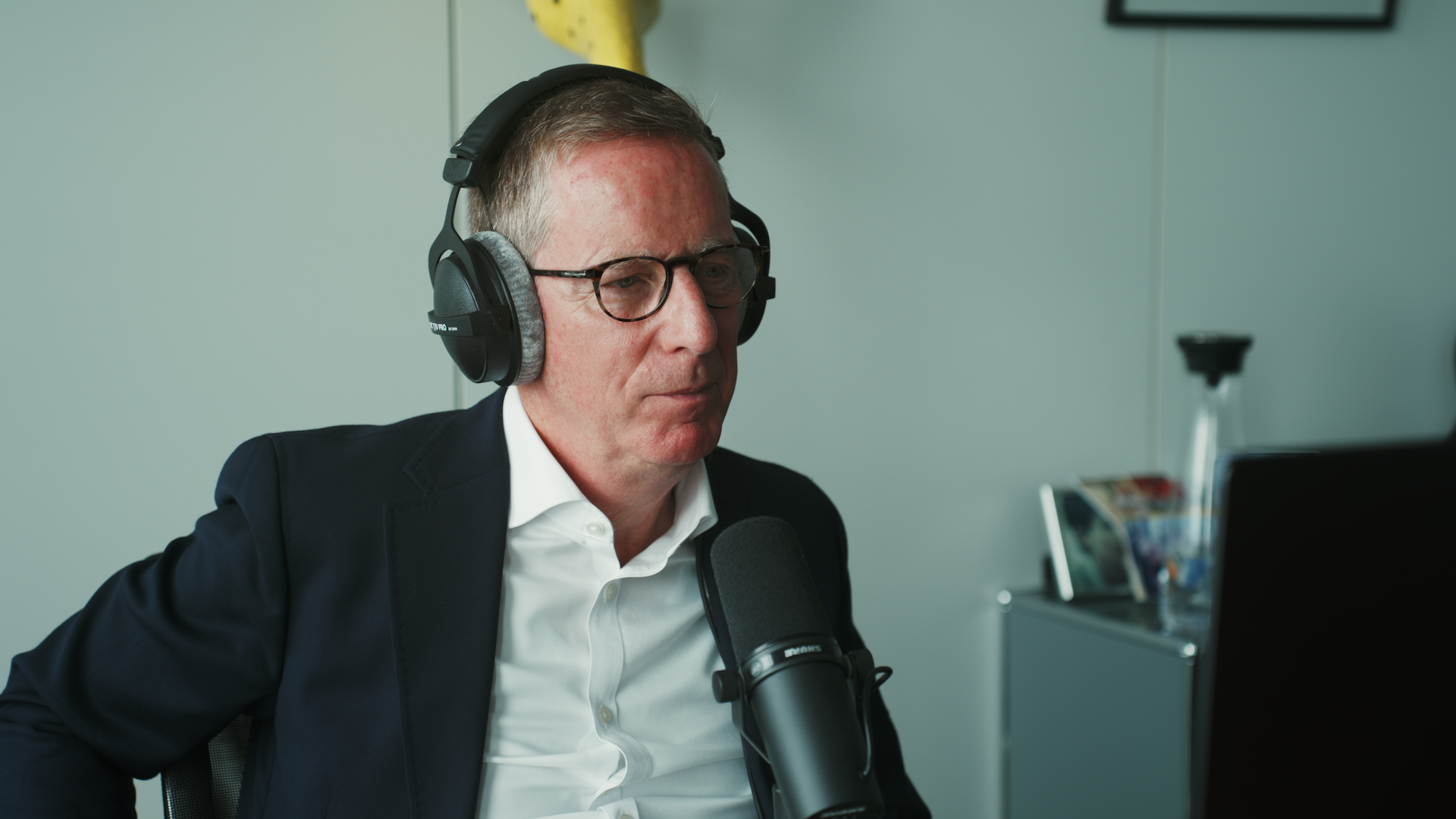Eine Person mit Kopfhörern in Hemd und Blazer sitzt an einem Mikrofon und hört zu.