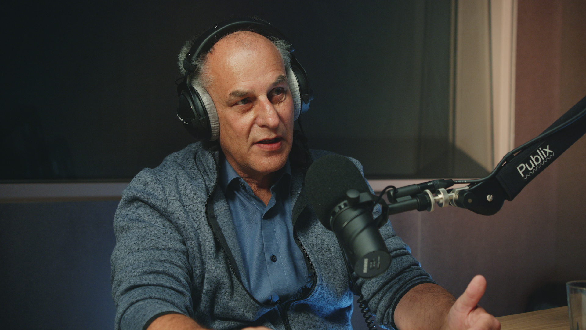 Eine Person sitzt mit Kopfhörer vor einem Mikrofon und spricht.