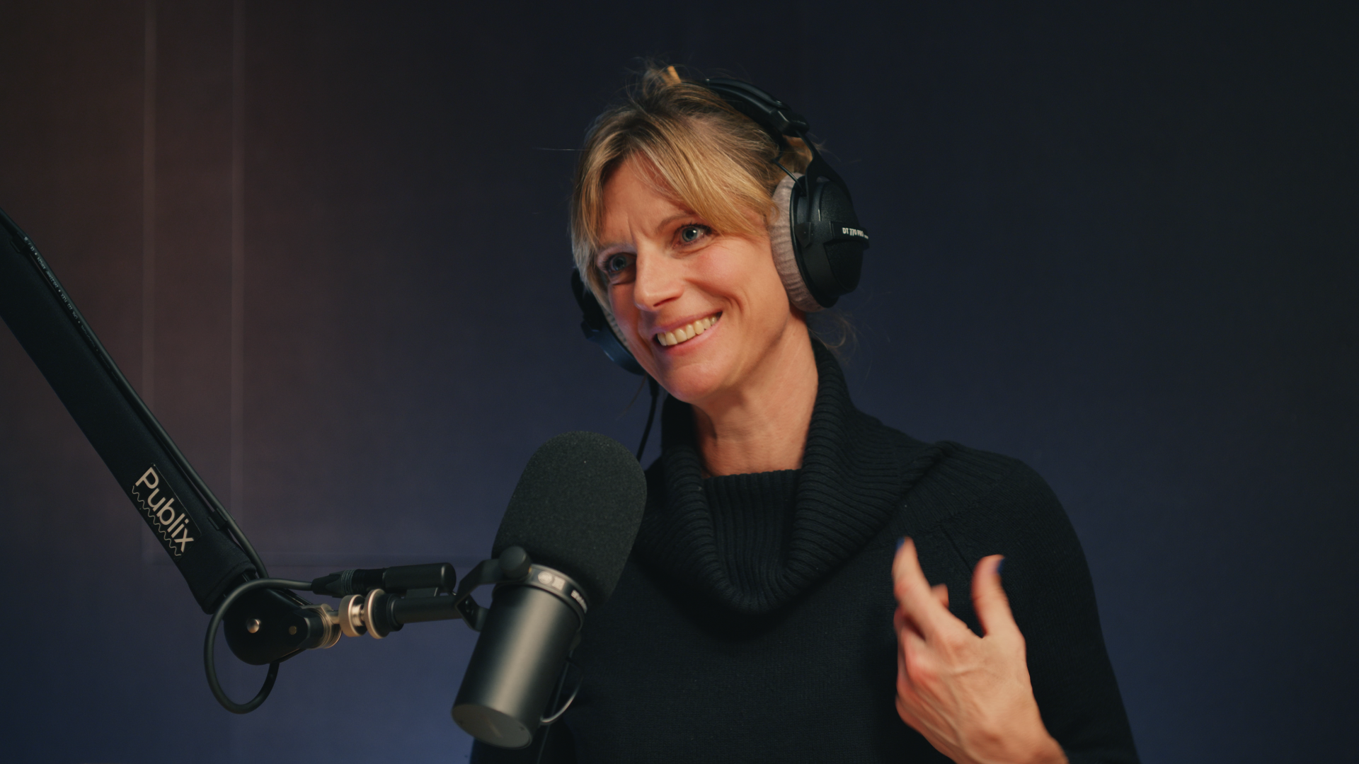 Eine Person mit Kopfhörern sitzt an einem Mikrofon und gestikuliert.