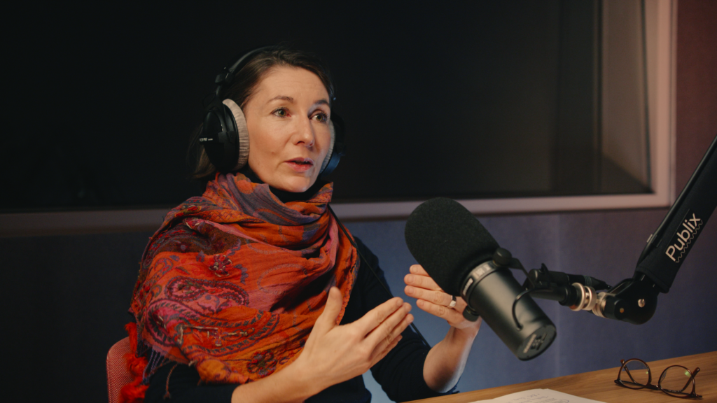 Eine Person mit Kopfhörern sitzt an einem Mikrofon und gestikuliert.