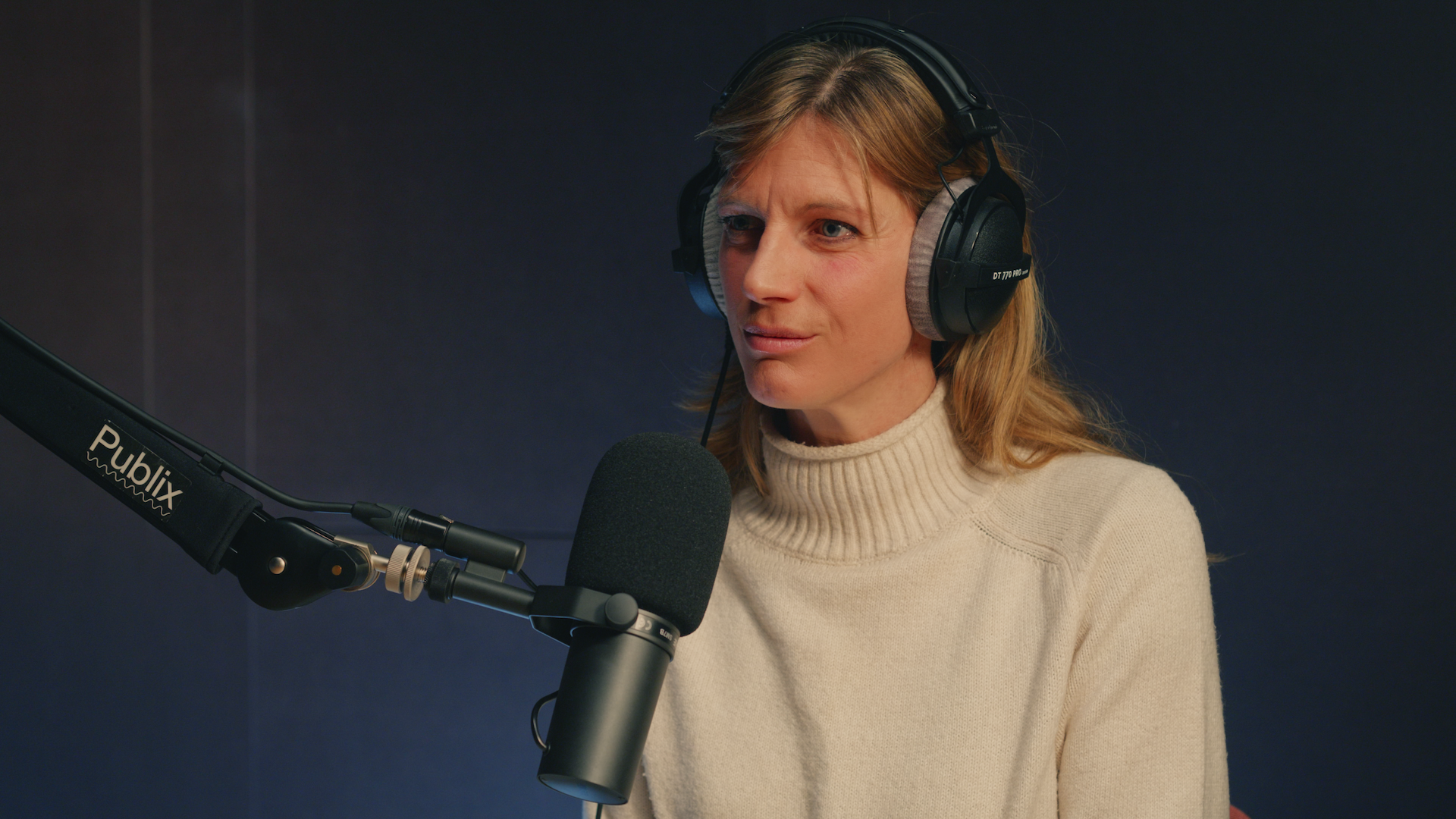 Eine Person in weißem Rollkragenpulli mit Kopfhörern vor einem großen Mikro