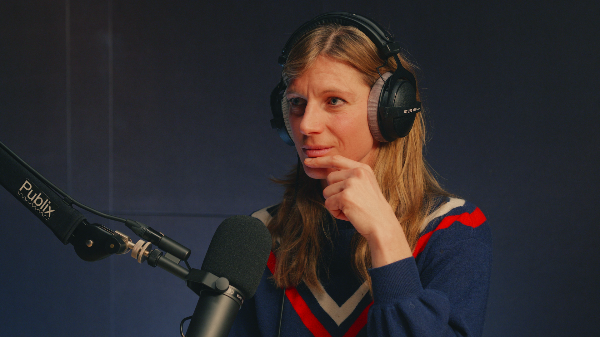 Eine Person sitzt mit Kopfhörer vor einem Mikrofon und spricht/hört zu.