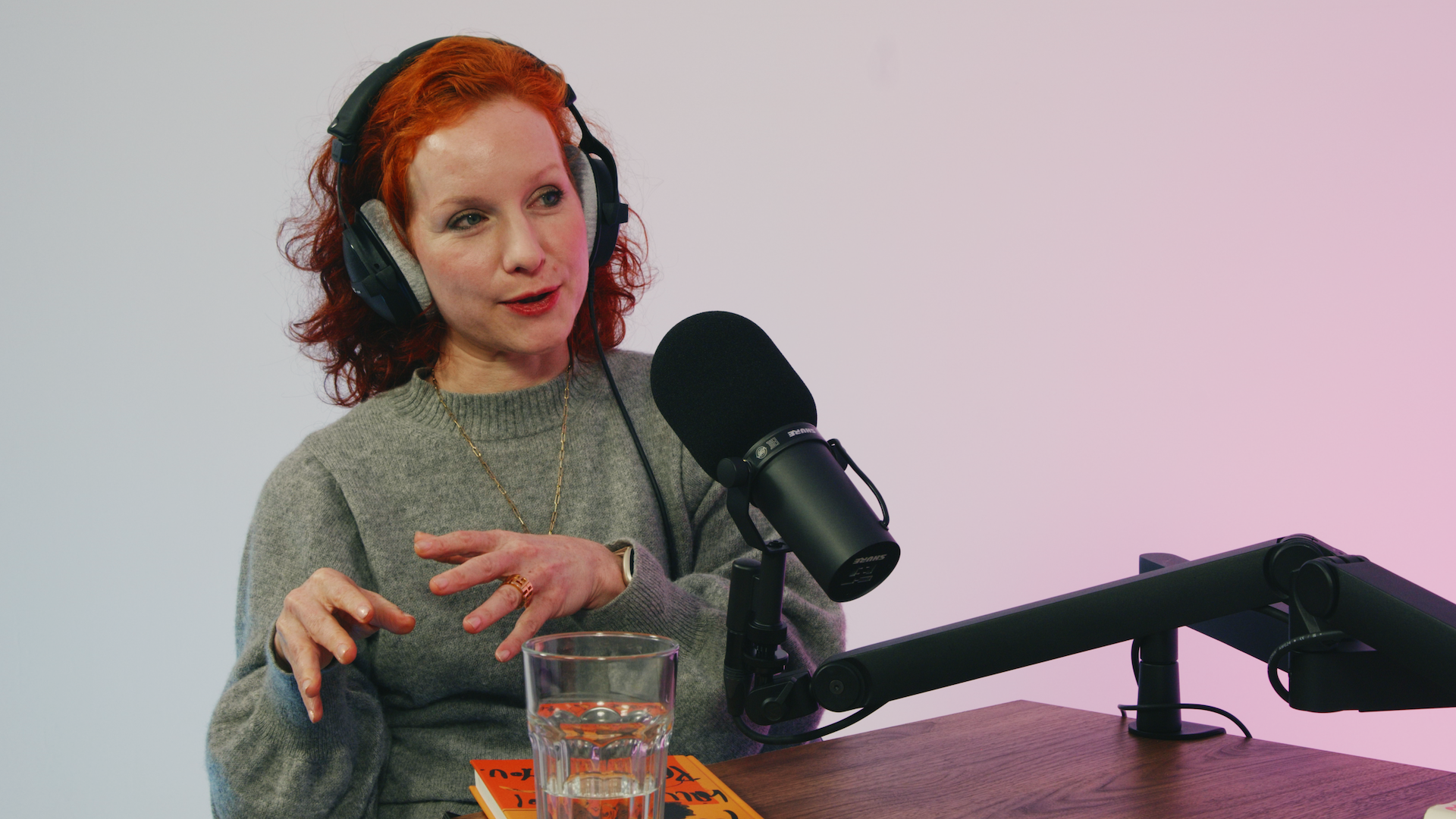 Eine Person sitzt mit Kopfhörer vor einem Mikrofon und spricht.