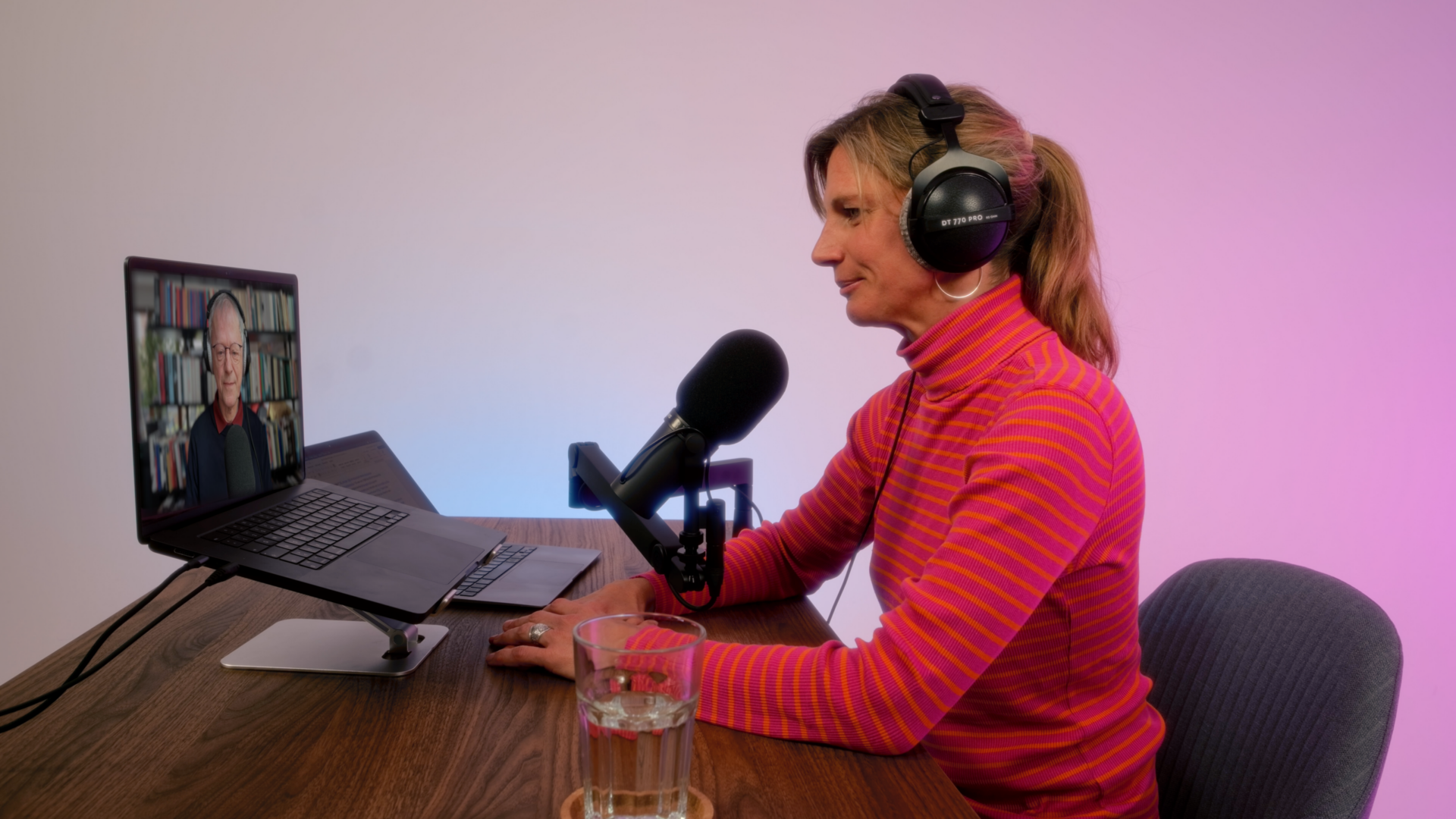 Eine Frau unterhält sich über Laptop und Mikrofon mit einem Mann, dessen Gesicht auf dem Bildschirm zu sehen ist.