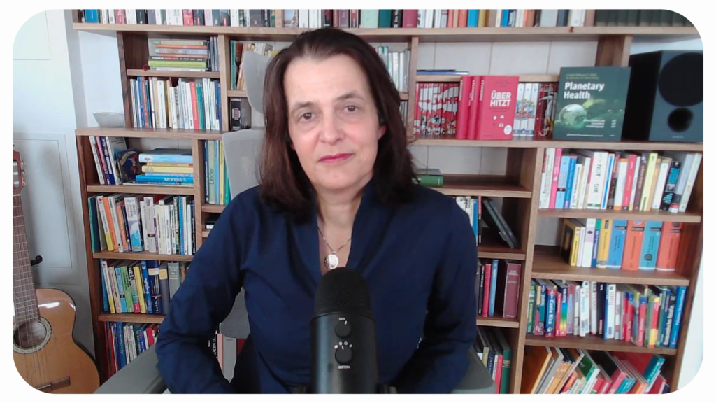 Eine Frau vor einem Bücherregal und mit einem Podcast-Mikrofon blickt in die Kamera.