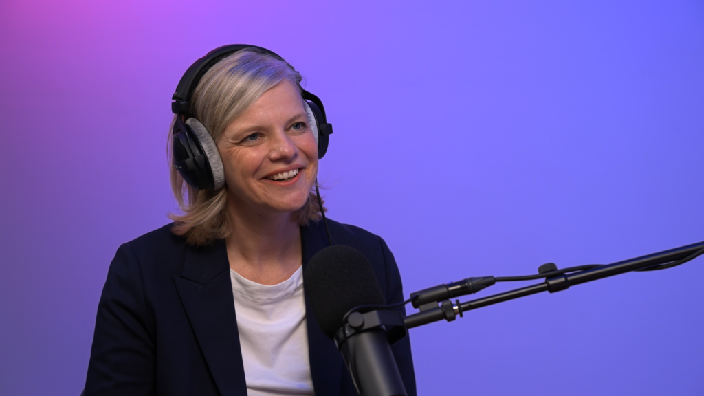 Frau mit Over-Ear-Kopfhörern vor einem Mikrofon in einem Studio mit violett-blauem Hintergrund.